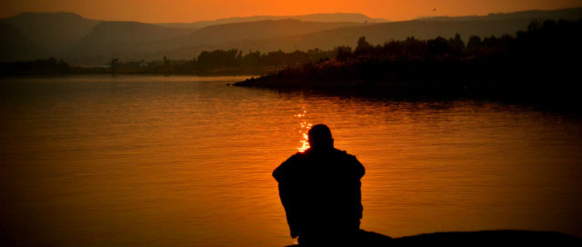 Mann sitzt bei Sonnenuntergang am See