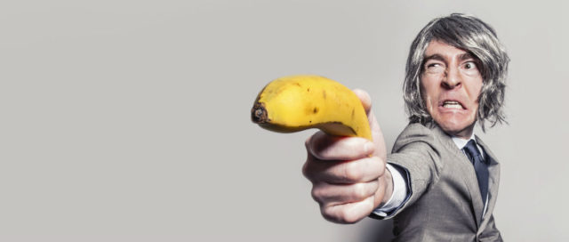 Mann zielt mit Banane als Waffe