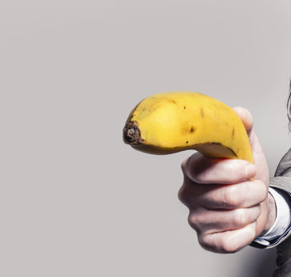 Mann zielt mit Banane als Waffe