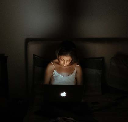 Frau sitzt auf Bett mit Laptop auf den Beinen