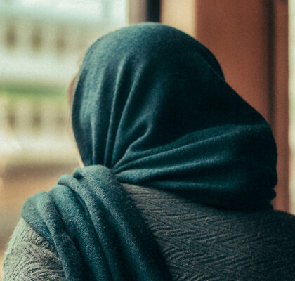 Frau mit Kopftuch schaut aus dem Fenster