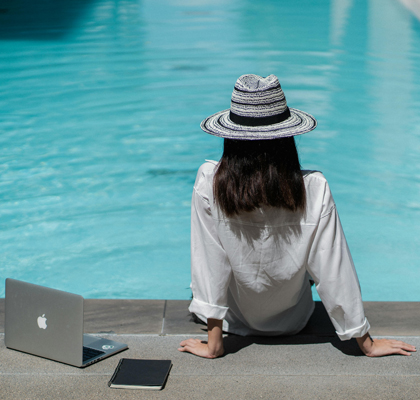 Frau sitzt mit Laptop und Notizbuch am Pool