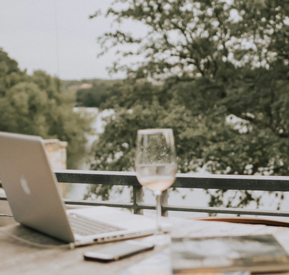 Laptop, Handy, Notzibuch und Weinglas auf einem Tisch am Meer