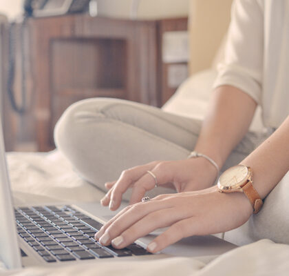 Frau sitzt mit Laptop auf Bett