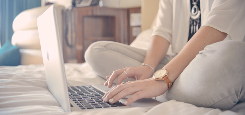 Frau sitzt mit Laptop auf Bett