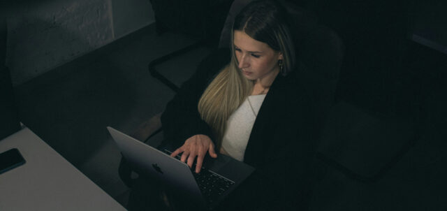 Eine Frau sitzt im dunklen Büro am Laptop